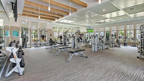 Ett modernt gym med olika typer av träningsutrustning, stora fönster och ett träpanelat tak.