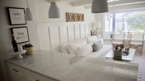 Een moderne keuken met een wit aanrecht, een witte bank en een eethoek met witte stoelen. Er hangen hanglampen boven de keuken en de eethoek.