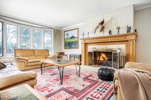 A cozy living room with a fireplace, leather furniture, and a large window. - Le Hudson Hideaway | Large Mid Century Bungalow with Ultimate Privacy on 1 Acre (Hudson)