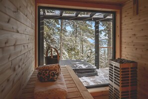 Une cabane en bois avec un banc, une cheminée et une vue sur des arbres couverts de neige.