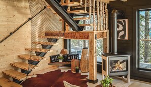 Un escalier en bois avec une rampe en métal noir, une cheminée et une fenêtre donnant sur les arbres.