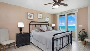 A bedroom with a bed, two nightstands, a chair, a ceiling fan, and a view of the ocean through a sliding door. - 7th-Floor Beachfront Marco Island Condo with Panoramic Ocean & Sunset Views (Marco Island)