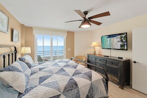 Een slaapkamer met een bed, plafondventilator, televisie, dressoir, stoel en uitzicht op de oceaan.