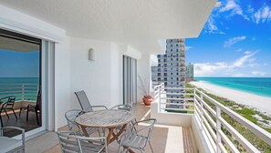 A balcony with a table and chairs, overlooking a beach and ocean. - 7th-Floor Beachfront Marco Island Condo with Panoramic Ocean & Sunset Views (Marco Island)