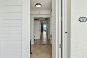 Een gang met een deur naar een kamer, een zichtbare deurbel en een nummerplaat aan de muur.