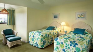 Ein Hotelzimmer mit zwei Betten, einem Korbstuhl, einem Deckenventilator und einem Fenster mit Vorhängen.