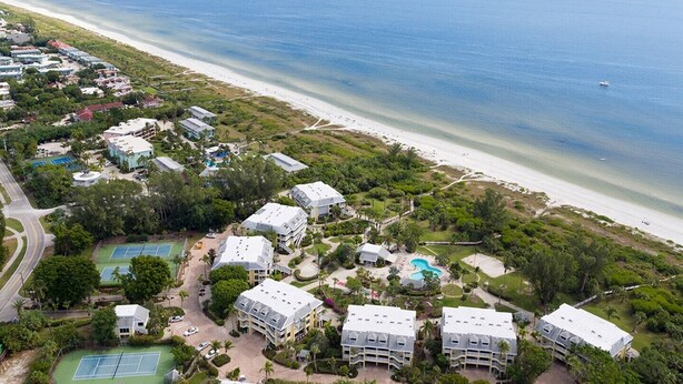 Ein Luftbild eines Küstenresorts mit mehreren Gebäuden, einem Strand und einem Tennisplatz.