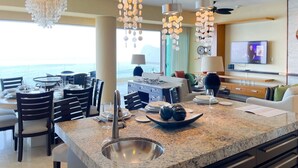 A modern kitchen with a granite countertop, stainless steel sink, and a dining area with round tables and chairs. - Luxury and quality located in the heart of Banderas Bay, Puerto Vallarta (Puerto Vallarta)