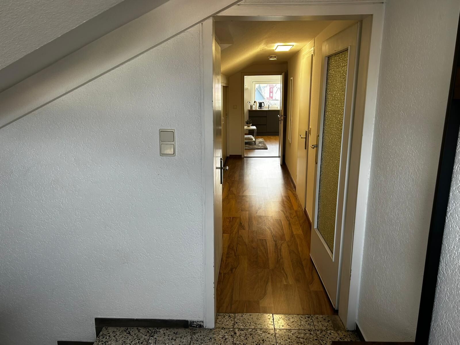 A hallway with a wooden floor leading to a kitchen area.