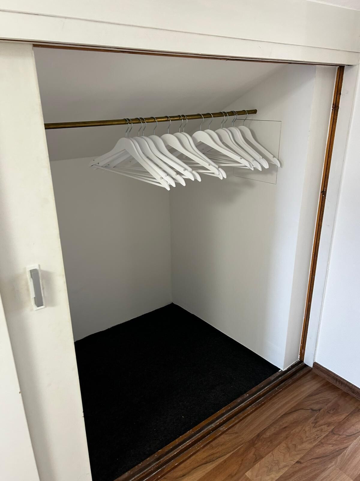 A walk-in closet with a black carpet floor and white hangers on a rod.