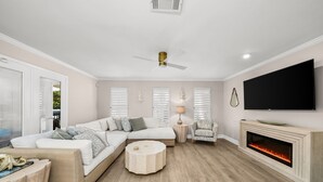 A modern living room with a sectional sofa, a round coffee table, a fireplace, and a flat-screen TV mounted on the wall. - Beach House · Private Beach · Private Pool & Backyard · Steps to Sand (Miramar Beach)