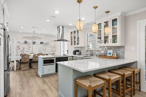 A modern kitchen with white cabinetry, a large island with bar stools, and pendant lighting. - Beach House · Private Beach · Private Pool & Backyard · Steps to Sand (Miramar Beach)