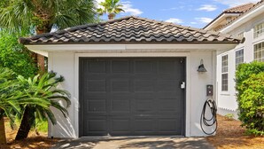 A residential garage with a dark door, a driveway, and a solar panel charger. - Beach House · Private Beach · Private Pool & Backyard · Steps to Sand (Miramar Beach)