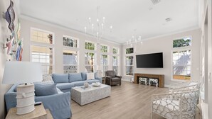 A spacious living room with a sectional sofa, a coffee table, a fireplace, and a television mounted on the wall. - Beach House · Private Beach · Private Pool & Backyard · Steps to Sand (Miramar Beach)