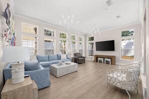 Ein geräumiges Wohnzimmer mit einer Eckcouch, einem Couchtisch, einem Kamin und einem an der Wand befestigten Fernseher.