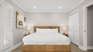 A bedroom with a large bed, two bedside tables with lamps, a wall-mounted picture, and a door. - Beach House · Private Beach · Private Pool & Backyard · Steps to Sand (Miramar Beach)
