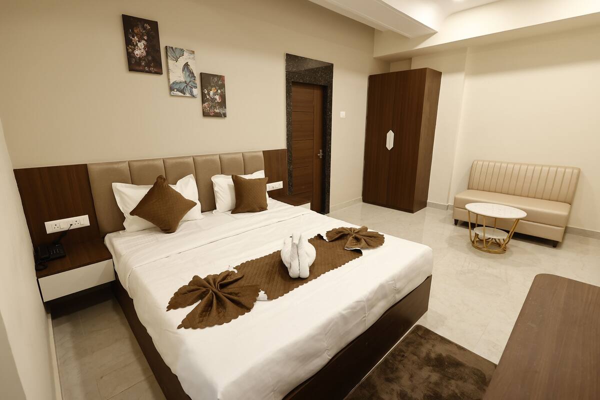 A hotel room with a large bed, a bedside table, a small round table, a sofa, and a door.