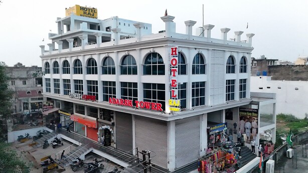 A hotel building with multiple floors, large arched windows, and a prominent sign reading "HOTEL RAJ ADARSH TOWER".