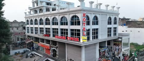 A hotel building with multiple floors, large arched windows, and a prominent sign reading "HOTEL RAJ ADARSH TOWER".