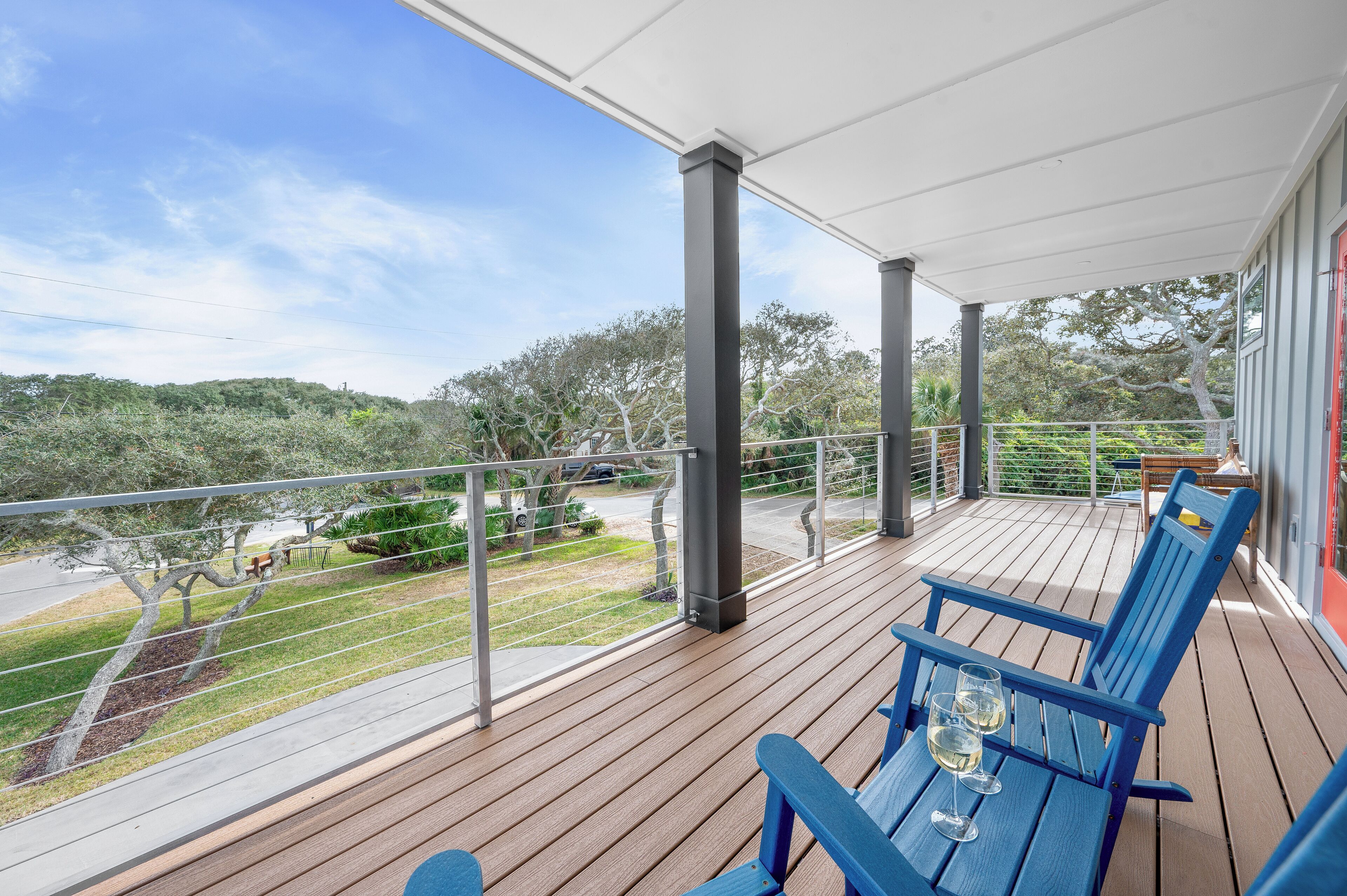 A wooden deck with blue chairs and a table, overlooking a landscaped area with trees and a road.