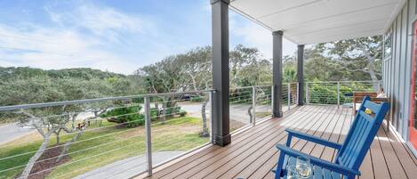 A wooden deck with blue chairs and a table, overlooking a landscaped area with trees and a road.