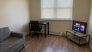 Una sala de estar con un sofá gris, una silla de oficina negra, una mesa de centro de madera y un televisor sobre un mueble.