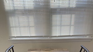 Un comedor con una mesa de madera y cuatro sillas, una ventana con persianas, y piso de madera.