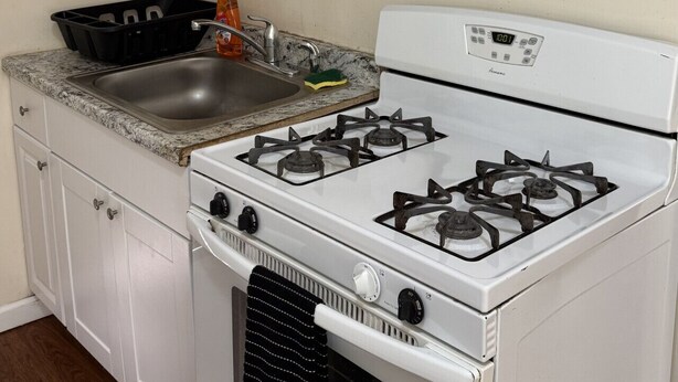 Una cocina con armarios blancos, estufa a gas, un lavabo y una cesta negra.