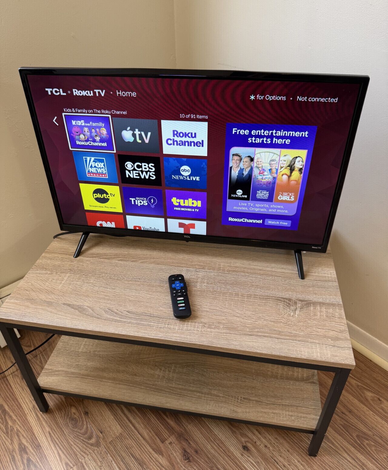 A TCL Roku TV on a wooden stand displaying various streaming channels.