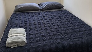 Una cama individual con colcha azul oscuro, dos almohadas y una toalla doblada.
