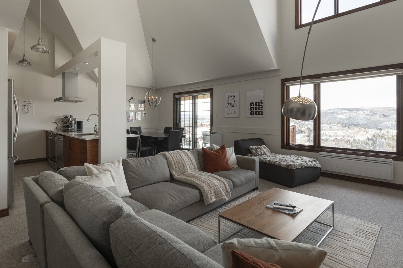 A spacious living area with a large gray sectional sofa, a coffee table, and a view of a snowy landscape through large windows.