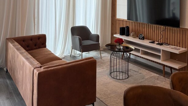 A modern living room with a brown leather sofa, a grey armchair, and a wooden entertainment unit with a flat-screen TV. - Magic Spring (Kissimmee)