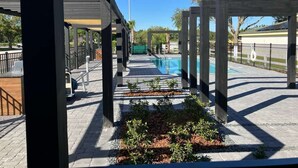 An outdoor swimming pool area with a covered walkway, benches, and a wooden pergola structure. - Magic Spring (Kissimmee)