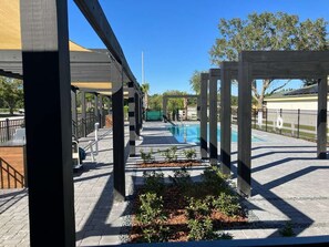 An outdoor swimming pool area with a covered walkway, benches, and a wooden pergola structure. - Magic Spring (Kissimmee)