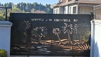 A metal gate with a landscape design, including palm trees and water, at the entrance to a property named SPRINGZ at 88 CROWHILL RD.