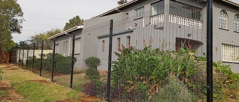 Een woongebouw met een grijze gevel, een zwart metalen hek en een tuin met diverse planten.