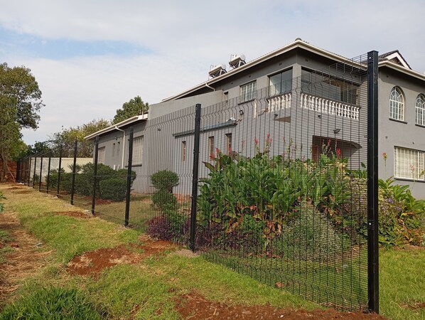 A residential building with a grey exterior, a black metal fence, and a garden area with various plants. - Perfect 7-bedroom house in Harare for your next family getaway (Harare)