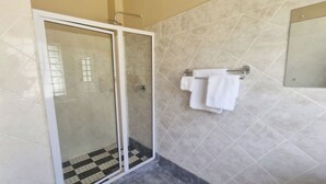 Un baño con cabina de ducha de vidrio, suelo de baldosas y toallero con toallas dobladas.