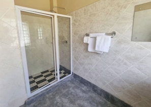 A bathroom with a glass shower enclosure, a tiled floor, and a towel rack with folded towels. - Perfect 7-bedroom house in Harare for your next family getaway (Harare)