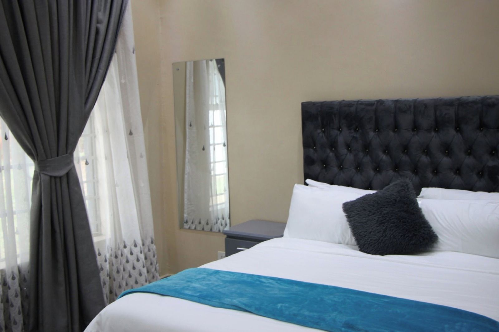 A hotel room with a large bed, a tufted headboard, a bedside table, and a window with curtains.