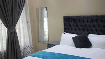 A hotel room with a large bed, a tufted headboard, a bedside table, and a window with curtains.