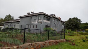 Una casa grande de color gris con un muro de piedra y una valla metálica al frente.