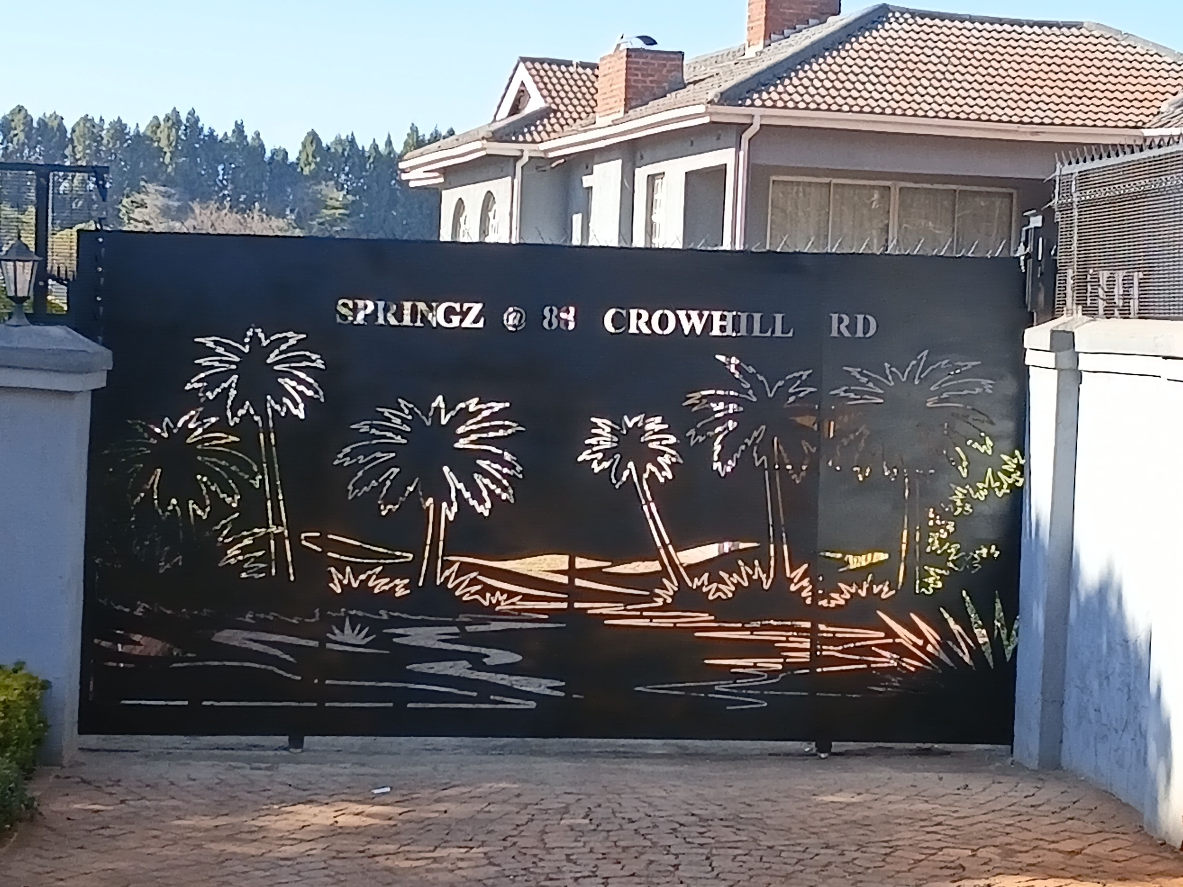 A gated entrance with a decorative metal gate featuring palm trees and a bridge.