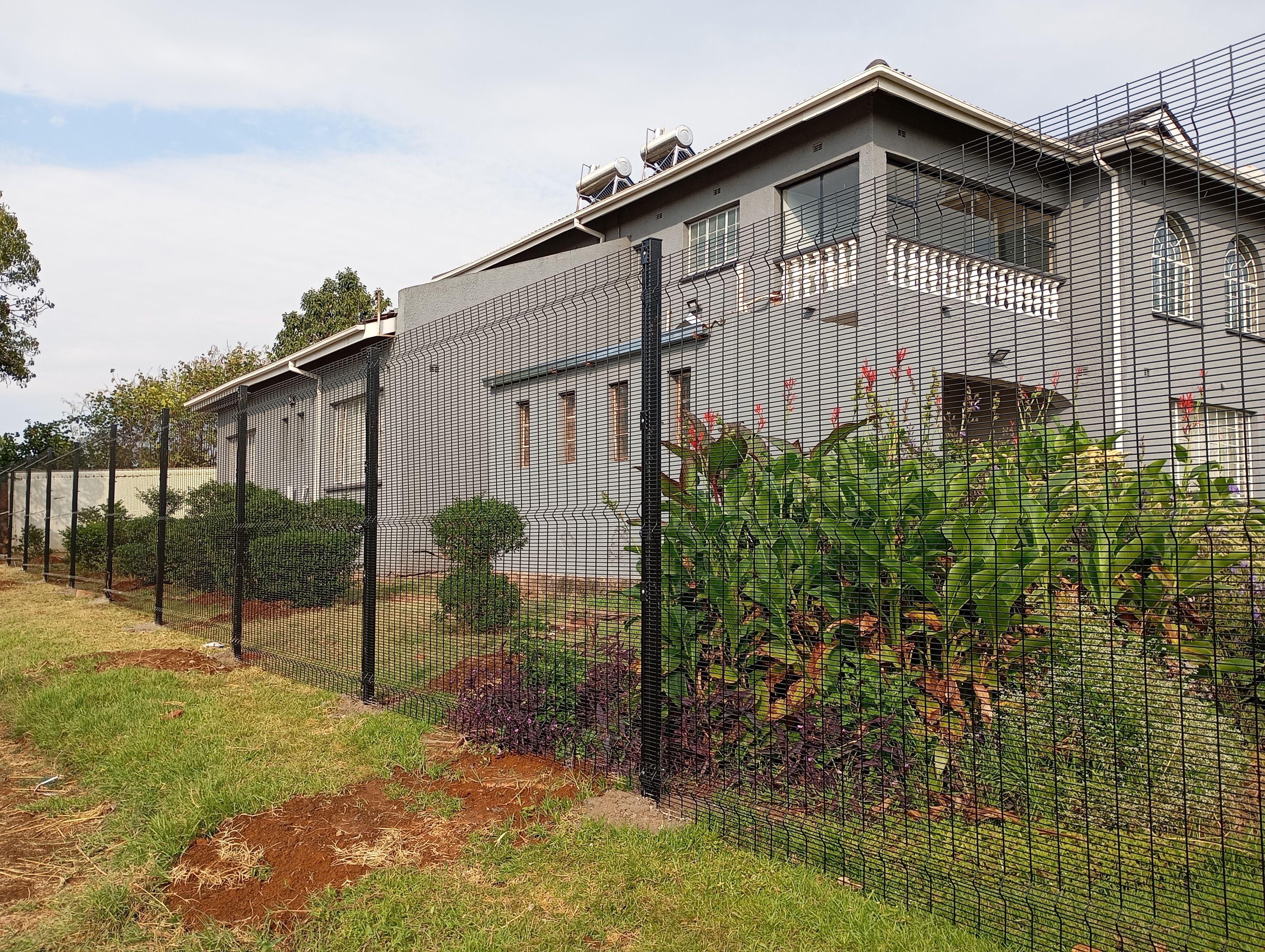 A residential building with a fenced yard, a small garden, and a satellite dish on the roof.