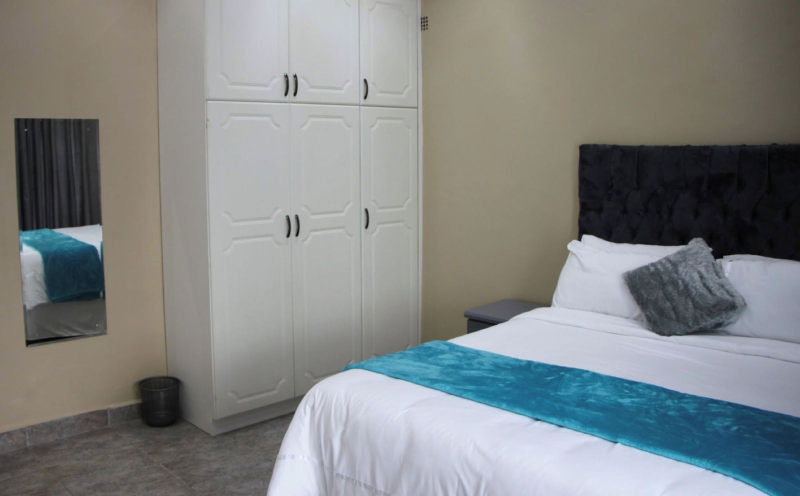 Une chambre d’hôtel avec un lit, une armoire, un miroir et une table de chevet.