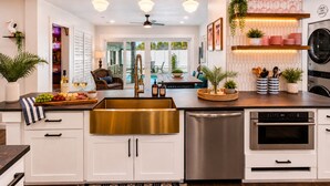Una cocina moderna con gabinetes blancos, electrodomésticos de acero inoxidable y una isla central con un lavamanos dorado.