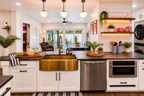 A modern kitchen with white cabinets, stainless steel appliances, and a central island with a gold sink. - Private Pool Oasis Near Anna Maria Island + Tiki Bar + Games + Sleeps 12 (Bradenton)