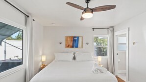 Un dormitorio ordenado con una cama grande, ventilador de techo, lámparas de noche y vistas al exterior.