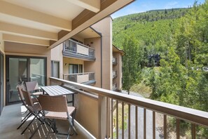 Un balcon avec une table et des chaises, donnant sur une colline boisée.