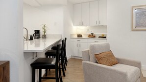 A modern kitchen with white cabinets, a dining area with black chairs, and a grey sofa with a brown pillow. - Fallridge Condo - Steps to Nordic Center & Bus (Vail)
